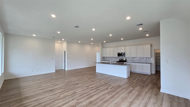 kitchen featuring white cabinets, backsplash, a kitchen island with sink, stainless steel appliances, and light wood-type flooring