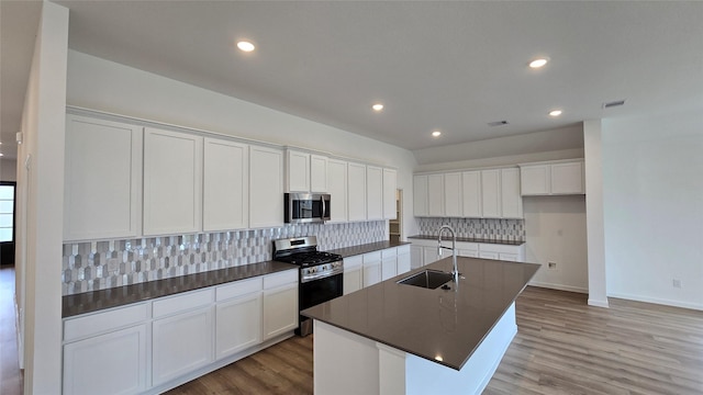 kitchen with sink, a kitchen island with sink, stainless steel appliances, white cabinets, and decorative backsplash