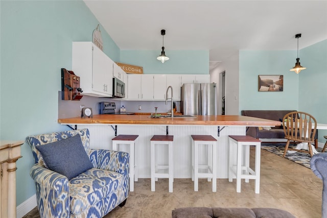 kitchen with white cabinetry, appliances with stainless steel finishes, a kitchen breakfast bar, kitchen peninsula, and pendant lighting