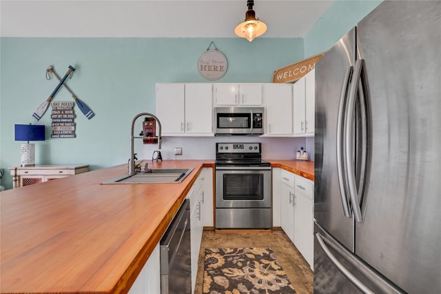 kitchen featuring decorative light fixtures, white cabinetry, sink, wooden counters, and stainless steel appliances