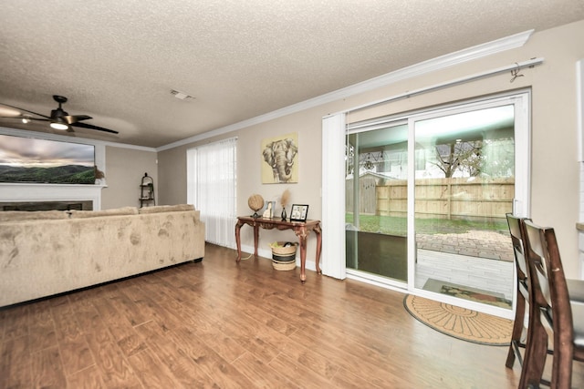 living room with hardwood / wood-style flooring, ceiling fan, ornamental molding, and a textured ceiling