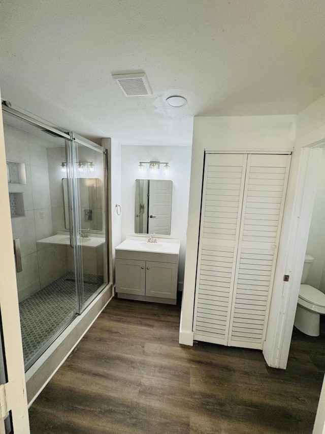 bathroom with hardwood / wood-style flooring, vanity, an enclosed shower, and toilet