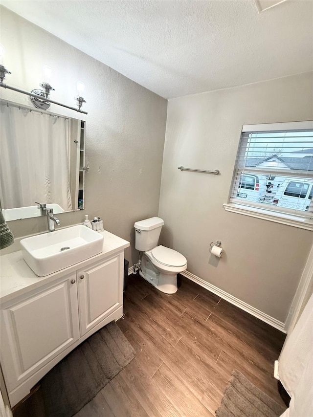 bathroom featuring wood-type flooring, toilet, vanity, and a textured ceiling