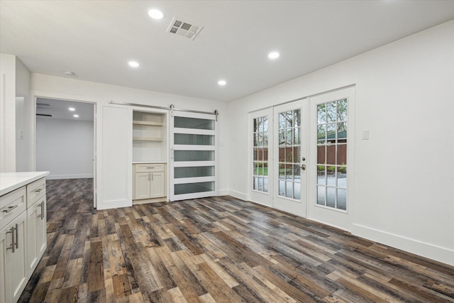 unfurnished living room with dark hardwood / wood-style floors, a barn door, and french doors