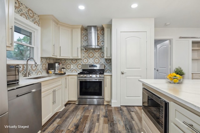 kitchen featuring sink, dark hardwood / wood-style flooring, wall chimney exhaust hood, stainless steel appliances, and cream cabinetry