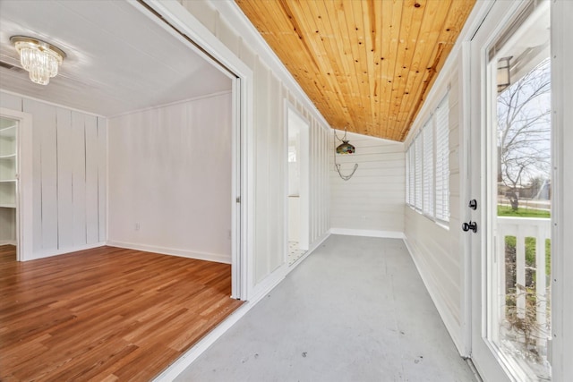 hallway featuring lofted ceiling, wood ceiling, concrete floors, and wood walls