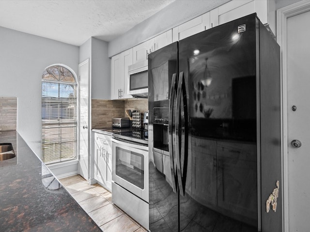 kitchen featuring appliances with stainless steel finishes, backsplash, a textured ceiling, white cabinets, and dark stone counters