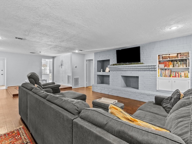 living room with brick wall, a brick fireplace, a textured ceiling, and light hardwood / wood-style floors