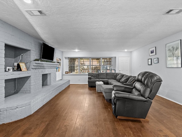 living room featuring a brick fireplace, dark wood-type flooring, and a textured ceiling