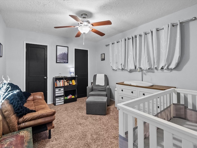 bedroom with a textured ceiling, a nursery area, ceiling fan, and carpet flooring