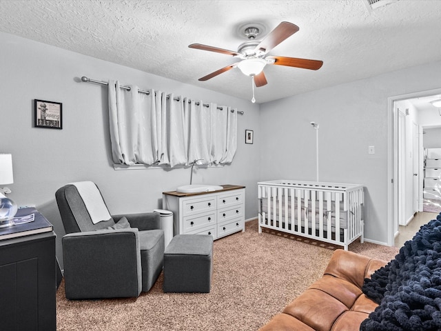 bedroom featuring a nursery area, carpet floors, a textured ceiling, and ceiling fan