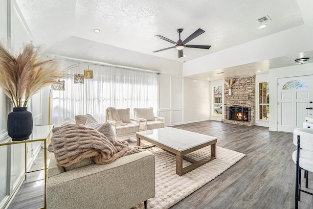 living room with a brick fireplace, a textured ceiling, a tray ceiling, dark hardwood / wood-style flooring, and ceiling fan