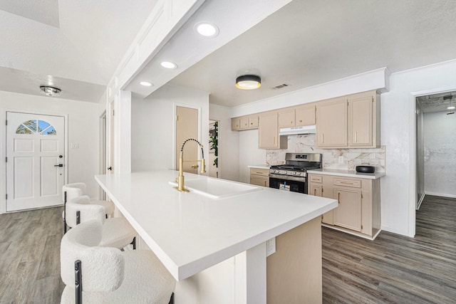 kitchen with light brown cabinetry, sink, backsplash, stainless steel gas range oven, and dark wood-type flooring