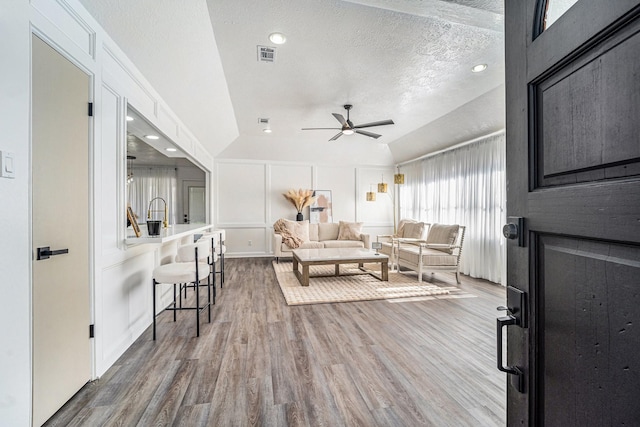 living room with hardwood / wood-style floors, vaulted ceiling, a textured ceiling, and ceiling fan