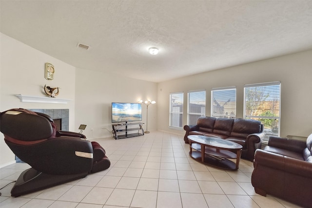 living room featuring a tiled fireplace, light tile patterned floors, a textured ceiling, and a healthy amount of sunlight