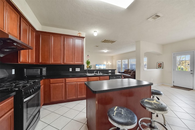 kitchen featuring stainless steel range with gas cooktop, a kitchen breakfast bar, a center island, and plenty of natural light