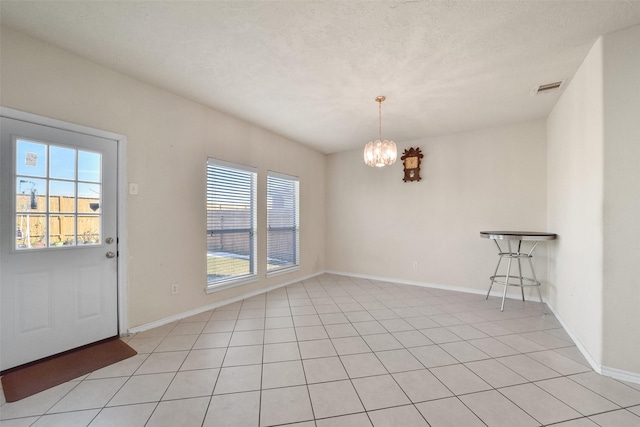 unfurnished dining area with an inviting chandelier, light tile patterned floors, and a textured ceiling