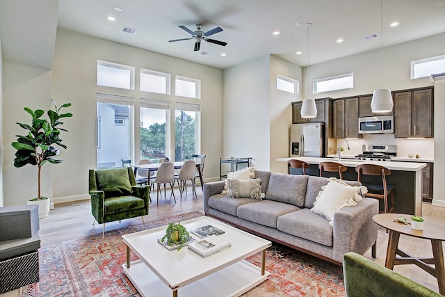 living room featuring sink, a towering ceiling, ceiling fan, and light wood-type flooring