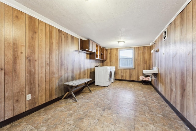 clothes washing area featuring sink, crown molding, a textured ceiling, separate washer and dryer, and wood walls