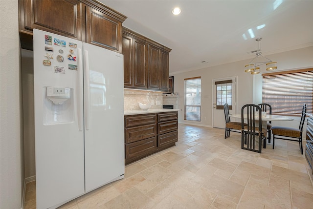 kitchen featuring decorative light fixtures, dark brown cabinets, ornamental molding, white refrigerator with ice dispenser, and decorative backsplash