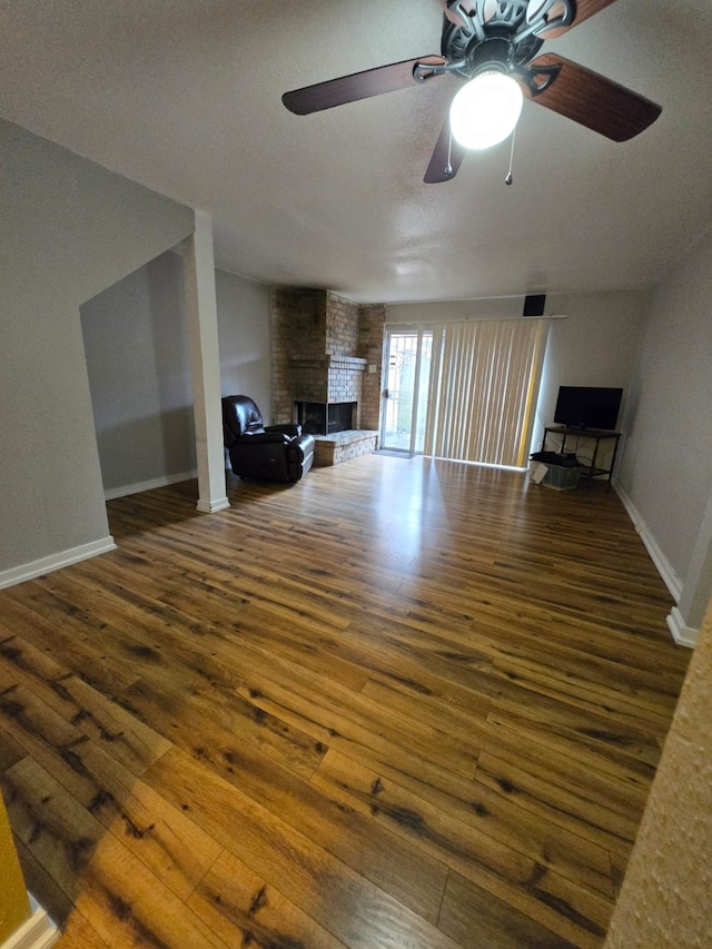 unfurnished living room featuring ceiling fan, dark wood-type flooring, and a fireplace