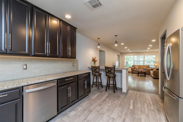 kitchen with light hardwood / wood-style flooring, appliances with stainless steel finishes, backsplash, light stone countertops, and decorative light fixtures