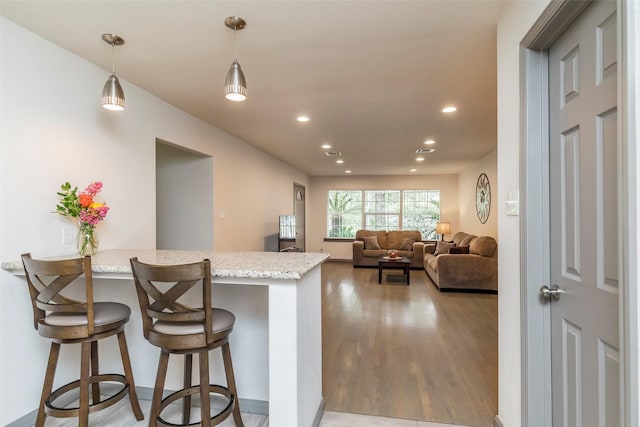 kitchen with kitchen peninsula, light stone counters, a kitchen breakfast bar, and decorative light fixtures