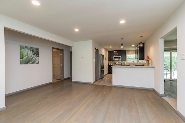 kitchen featuring sink, appliances with stainless steel finishes, backsplash, kitchen peninsula, and light wood-type flooring