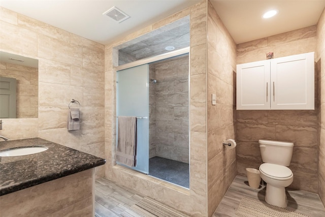 bathroom with hardwood / wood-style floors, tile walls, vanity, walk in shower, and toilet