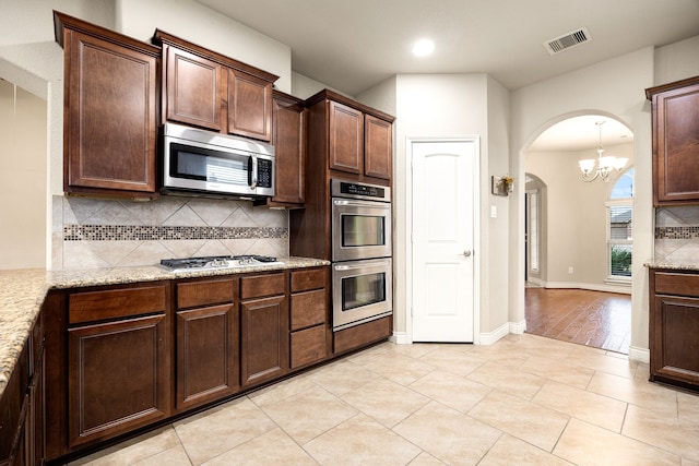 kitchen featuring decorative backsplash, light tile patterned floors, stainless steel appliances, light stone countertops, and dark brown cabinets