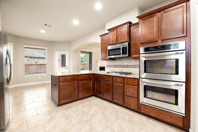 kitchen featuring appliances with stainless steel finishes, decorative backsplash, light tile patterned floors, kitchen peninsula, and light stone countertops