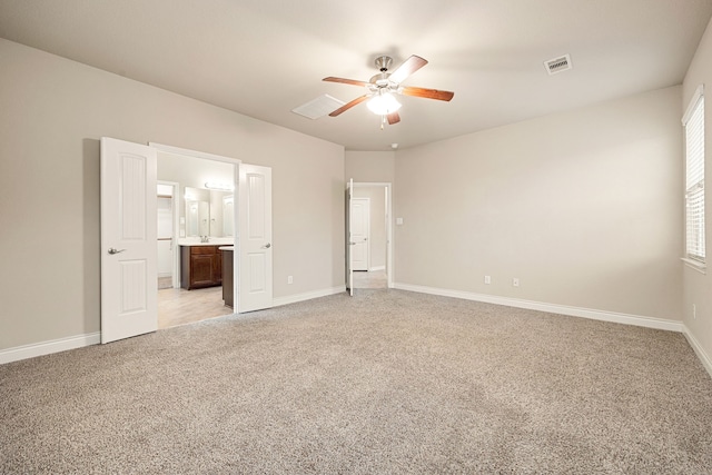 unfurnished bedroom with multiple windows, ensuite bathroom, light carpet, and ceiling fan