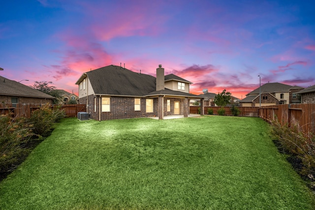 back house at dusk featuring a patio, cooling unit, and a lawn