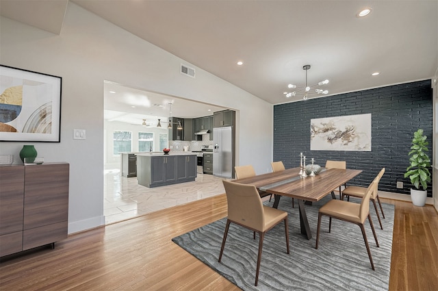 dining area featuring brick wall, lofted ceiling, an inviting chandelier, and light hardwood / wood-style flooring