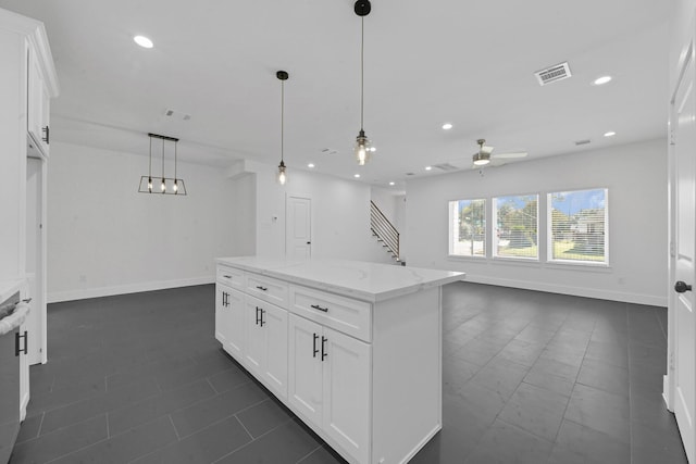 kitchen with light stone countertops, a center island, white cabinets, and decorative light fixtures