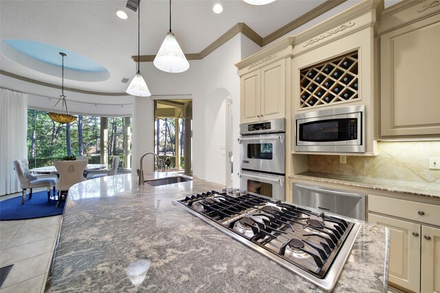 kitchen with pendant lighting, stainless steel appliances, light stone countertops, cream cabinets, and decorative backsplash