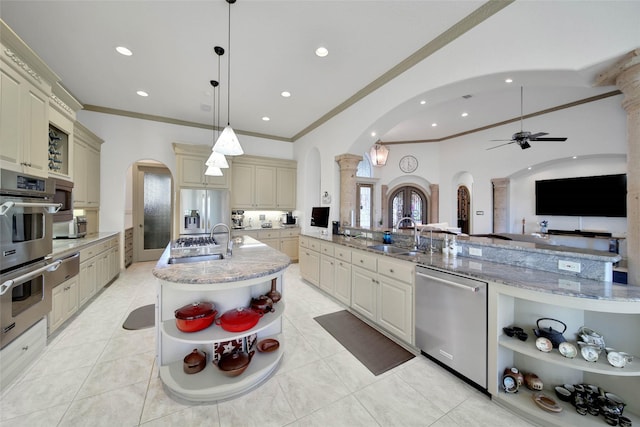 kitchen with sink, appliances with stainless steel finishes, hanging light fixtures, light stone countertops, and cream cabinetry