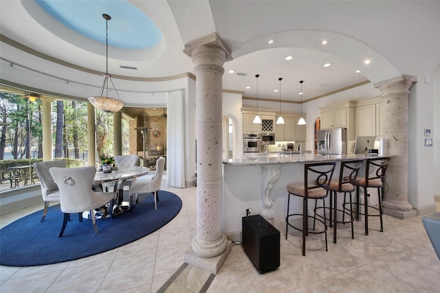 kitchen with ornate columns, decorative light fixtures, kitchen peninsula, stainless steel appliances, and light stone countertops