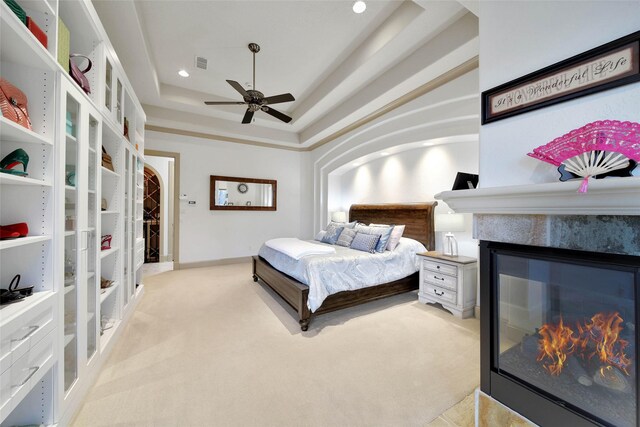 bedroom with light colored carpet, ceiling fan, and a tray ceiling