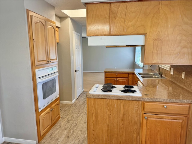 kitchen with light hardwood / wood-style floors, white appliances, kitchen peninsula, and sink