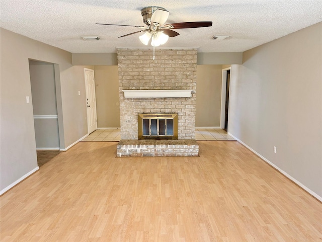 unfurnished living room featuring ceiling fan, a fireplace, light hardwood / wood-style floors, and a textured ceiling