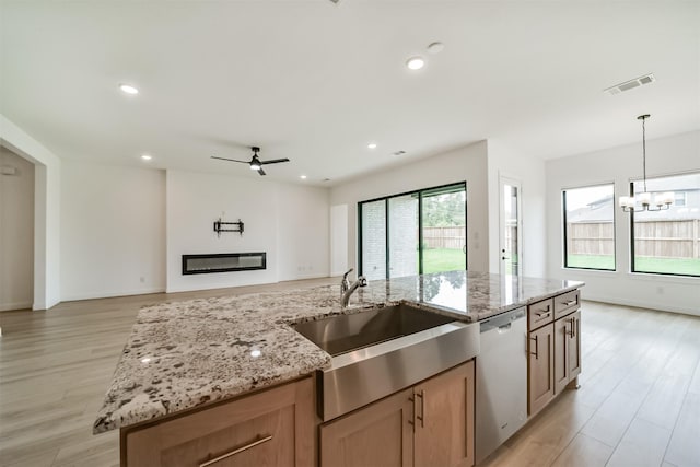 kitchen with dishwasher, light stone countertops, a kitchen island with sink, and sink