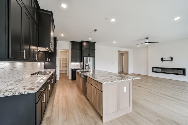 kitchen featuring light stone counters, a fireplace, an island with sink, and tasteful backsplash