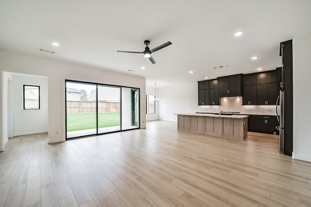 kitchen featuring stainless steel fridge, ceiling fan, hanging light fixtures, backsplash, and an island with sink