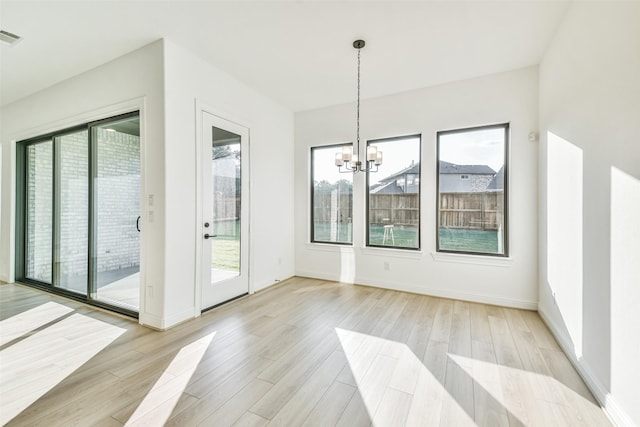 unfurnished dining area featuring a healthy amount of sunlight, an inviting chandelier, and light hardwood / wood-style floors