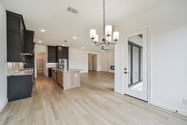 kitchen featuring tasteful backsplash, light stone counters, stainless steel fridge, an island with sink, and pendant lighting