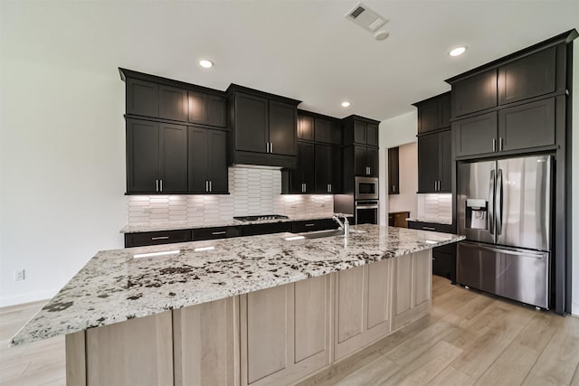 kitchen with sink, stainless steel appliances, a spacious island, light stone counters, and light wood-type flooring