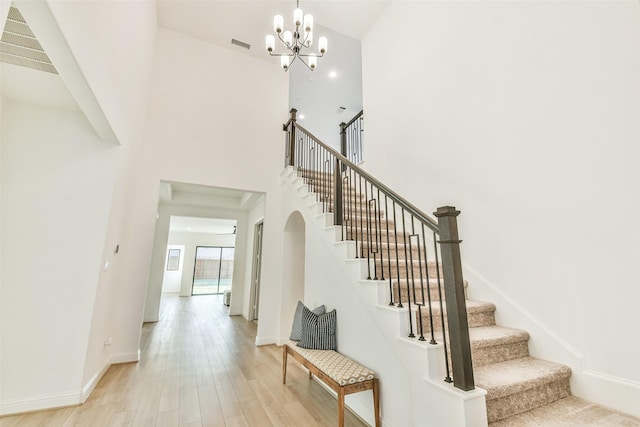 stairway featuring a notable chandelier, wood-type flooring, and a high ceiling