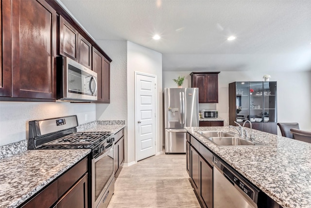 kitchen with appliances with stainless steel finishes, sink, dark brown cabinetry, light stone counters, and light hardwood / wood-style flooring