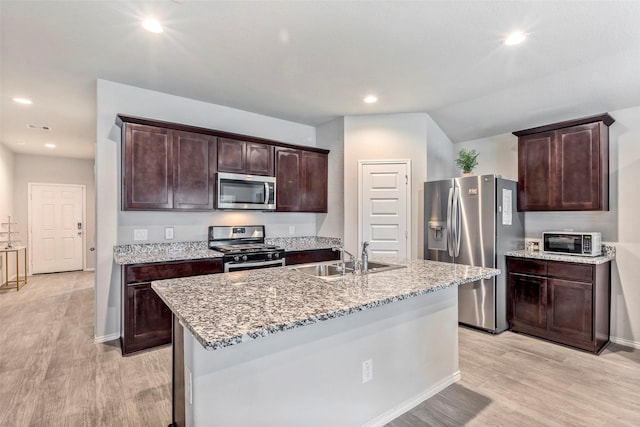 kitchen featuring dark brown cabinetry, sink, light wood-type flooring, appliances with stainless steel finishes, and an island with sink